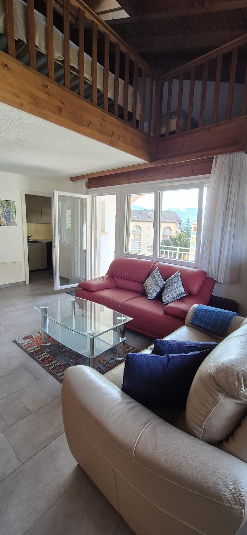 living room with a sofa set, glass table, rug, balcony, wooden beams