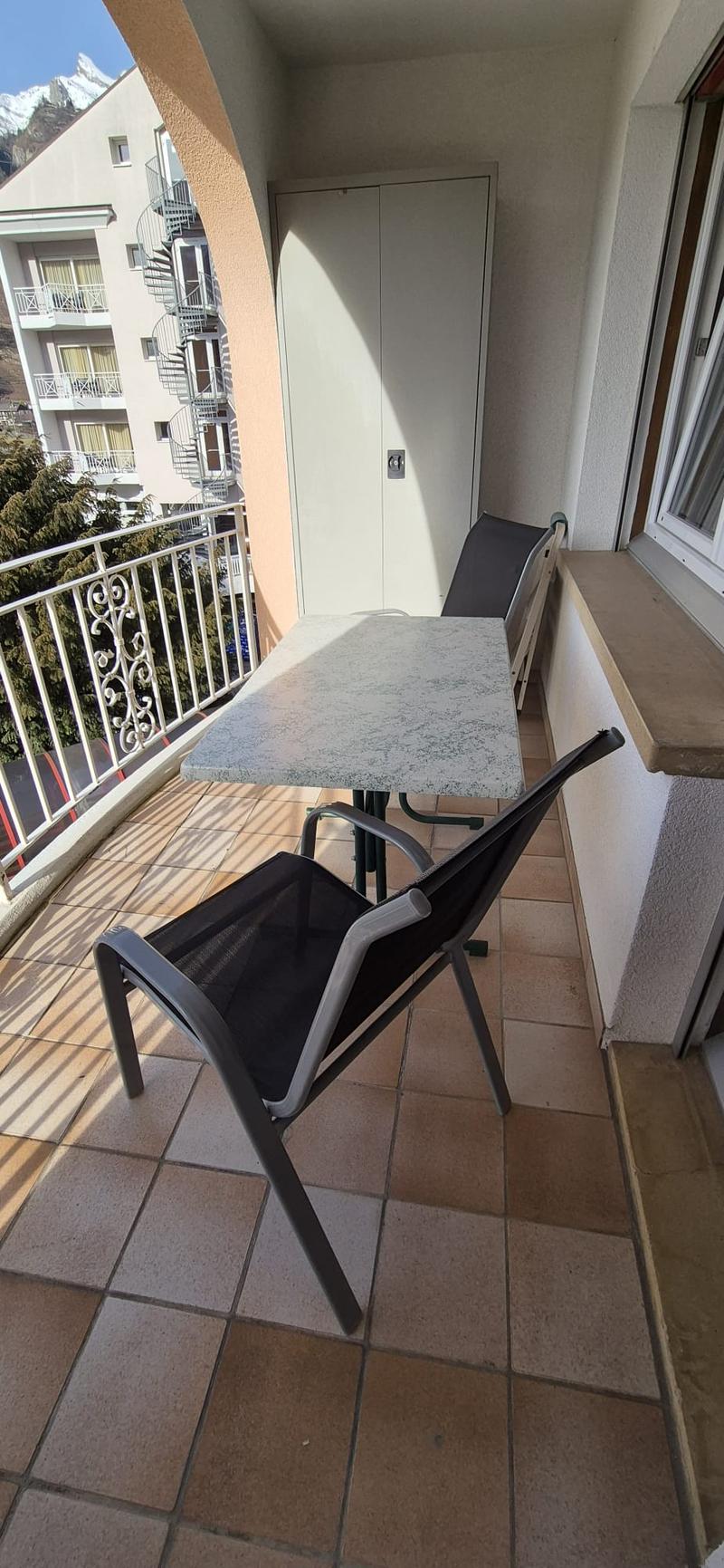 A balcony with chairs and a table. Behind the balcony there is a view of the mountains.