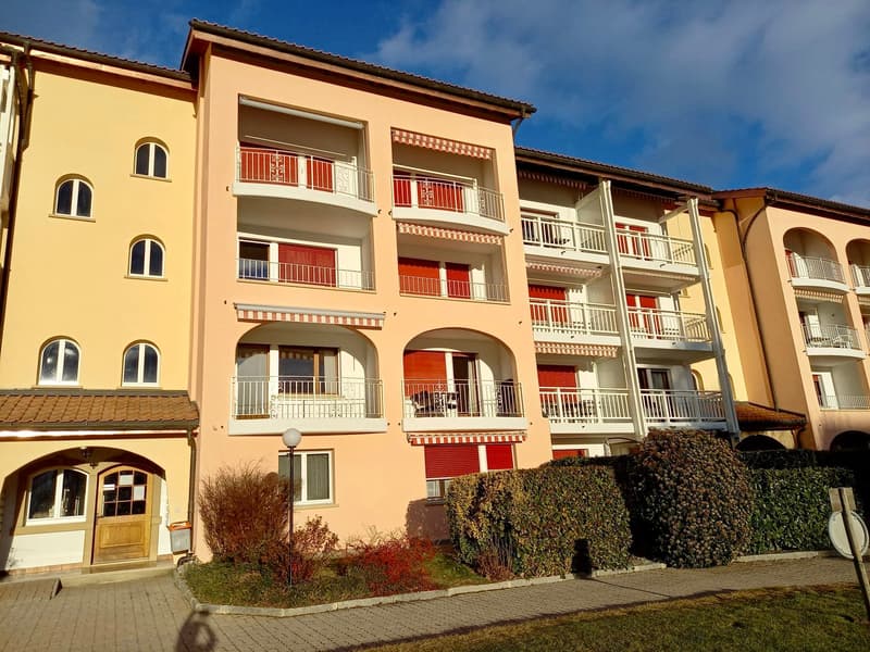 Three story apartment building, beige walls, red shutters, balconies, street lamp