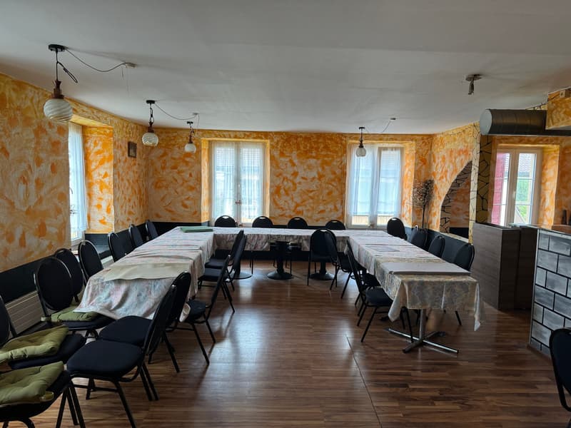large open room, long dining tables, chairs with cushions, yellow walls, windows, lamps