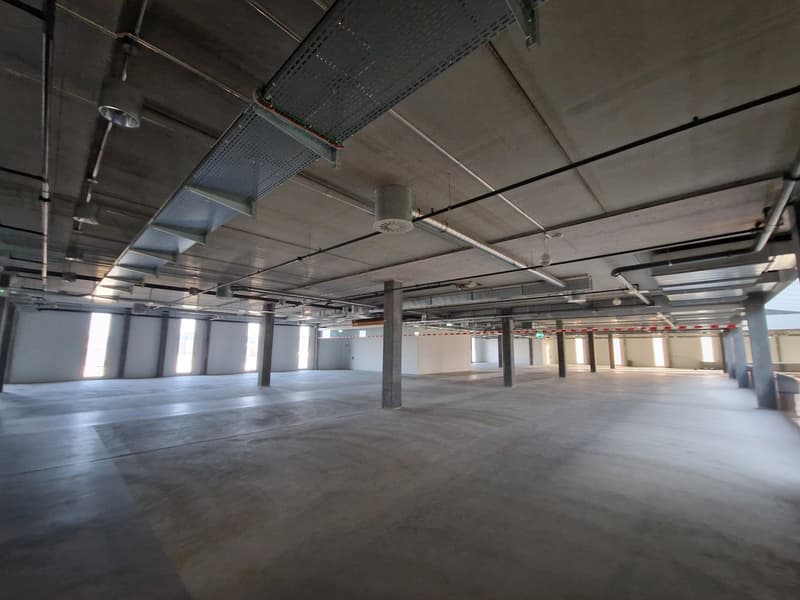 Open floor space, visible steel beams, multiple windows, ventilation systems, no furniture or decorations