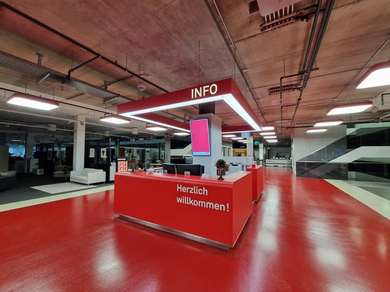 Open space, modern design, red floor, white walls, large red information desk, white reception area, multiple monitor displays, welcome message on desk