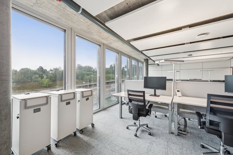 open office layout, large windows, desks, rolling office carts, chairs