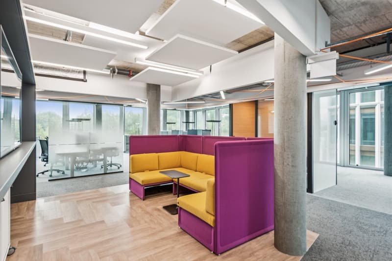 modern office, wooden floors, suspended ceiling, glass partitions, purple and yellow seating, concrete column, table, lights