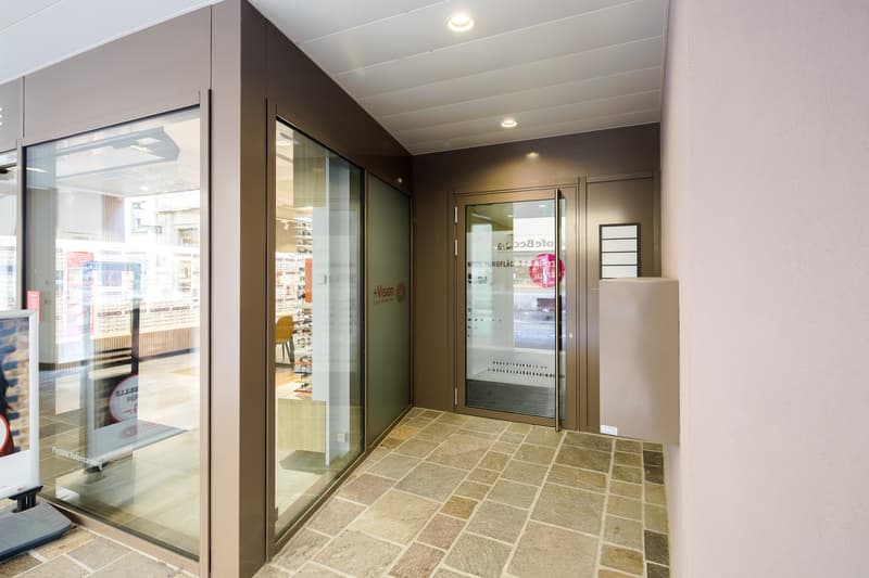 Main entrance of a building with glass doors, stone flooring, and a corridor