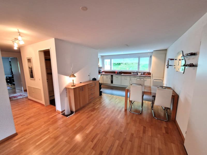 Spacious open-plan kitchen with hardwood floors, white cabinets, stainless steel appliances including a dishwasher, and a dining area with a table and chairs.