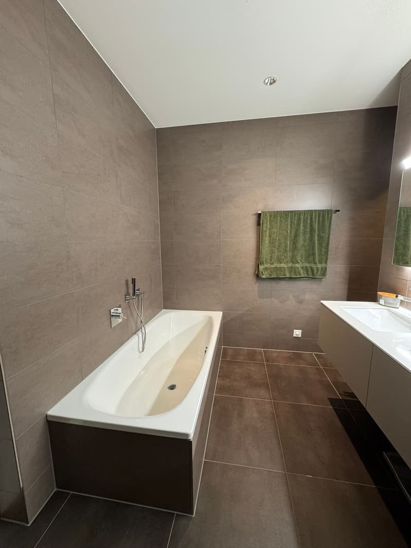 bathroom with bathtub and modern design, green towel, tiled floor and wall, double sink
