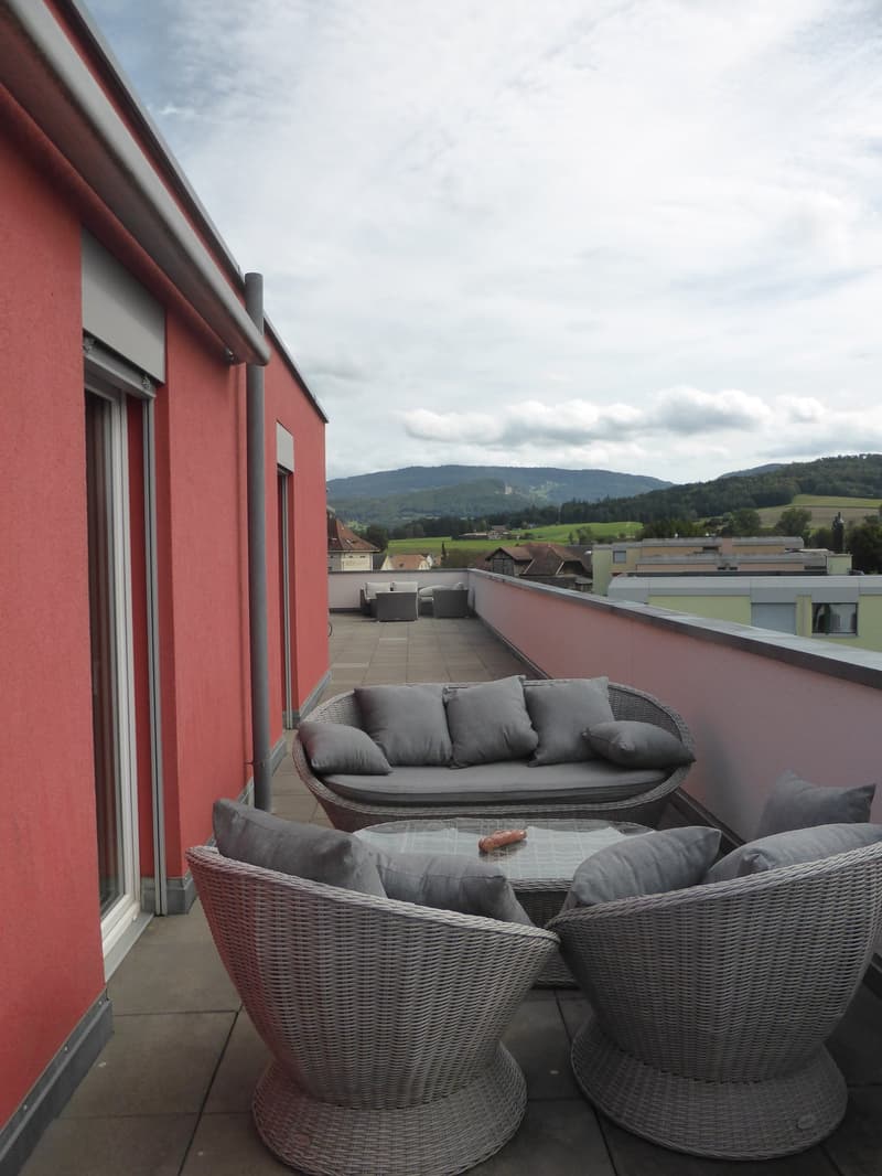 furnished balcony, wicker furniture, grey cushions, round coffee table, glass top, red walls, mountains in the distance