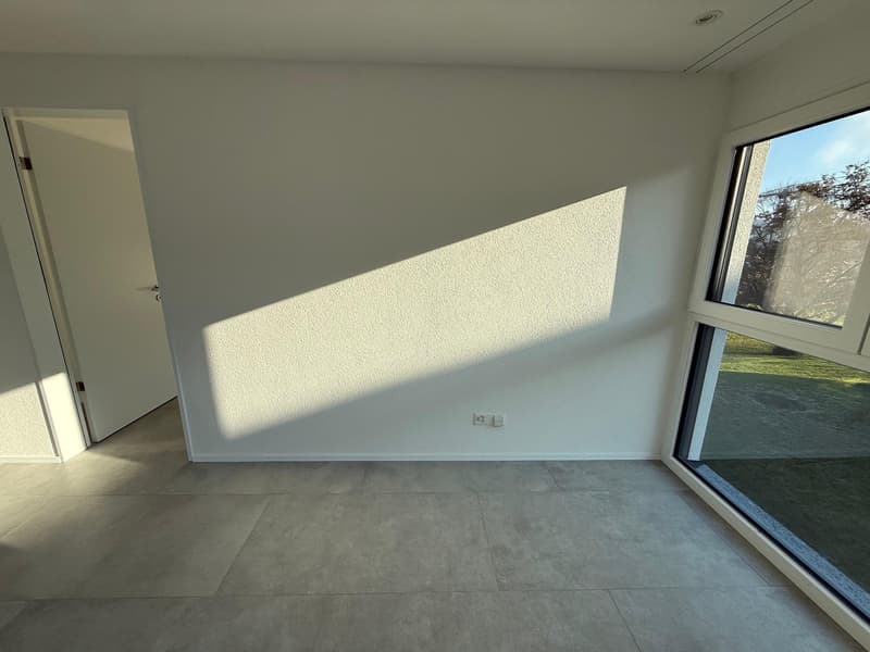 Empty room with white walls, gray floor, large window, and an open door.