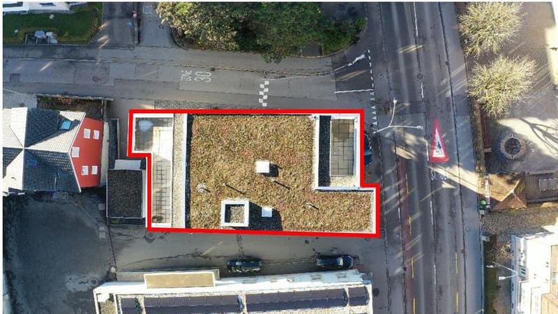 House with a green roof, solar panels on the roof, surrounded by roads, two cars parked in front