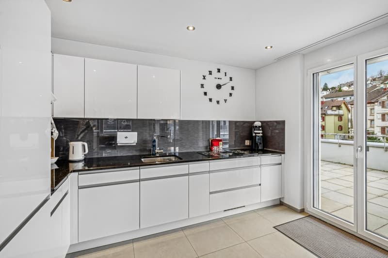 modern kitchen with white cabinets, black countertops, stainless steel appliances, large windows, balcony