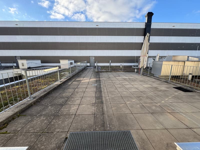 Industrial area rooftop with tiled flooring, metal railings, metal grate, and a street umbrella.