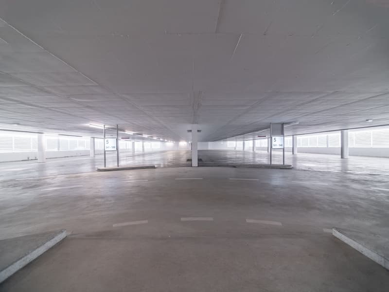 Underground parking space with white ceiling, concrete floor, white markings on the floor, white pillars with signages