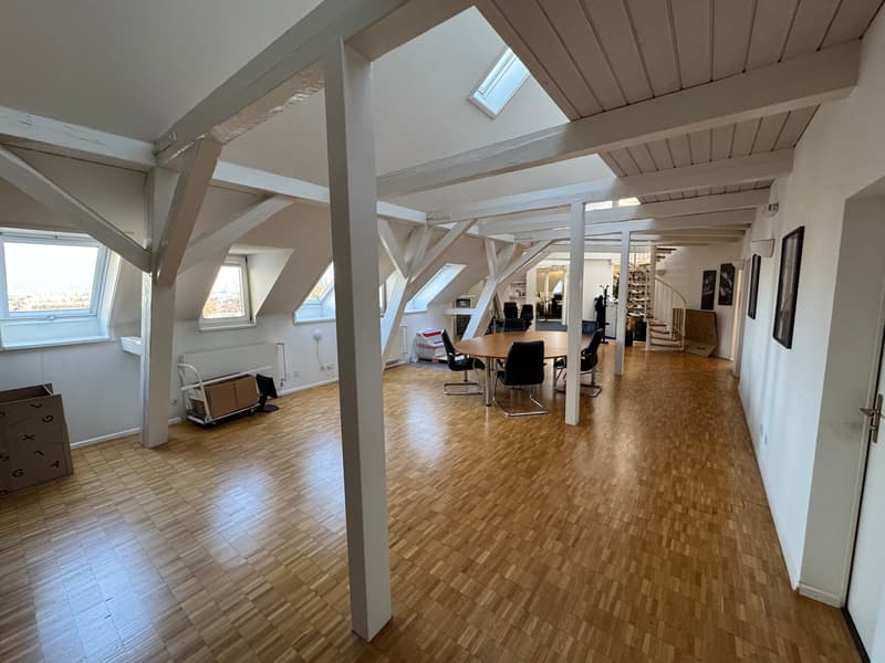 Large room with wooden floors, wooden beam ceiling, several windows, table, chairs, open layout, minimalistic