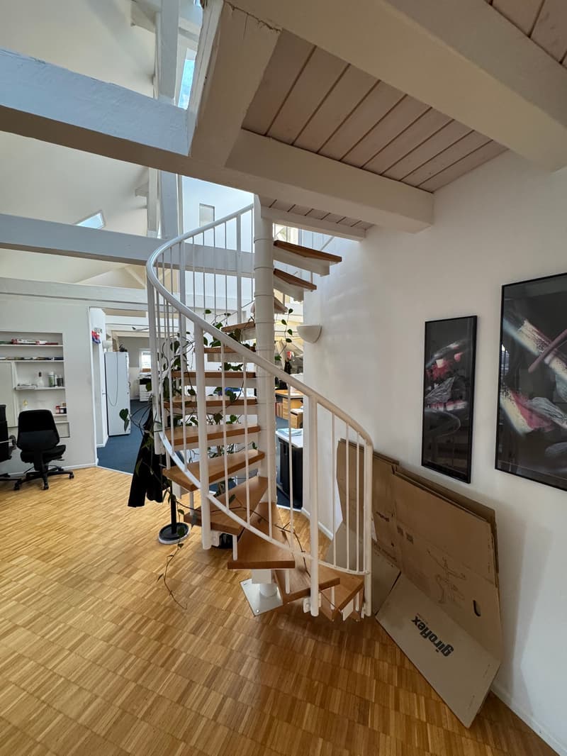Open area with wooden floor, spiral staircase, white walls, and storage boxes