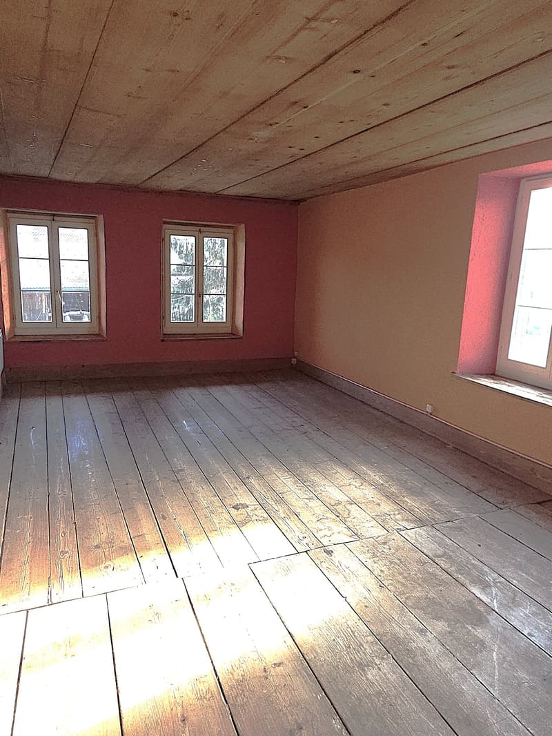 Empty room with wooden floor, red and beige painted walls, two windows with wooden frames