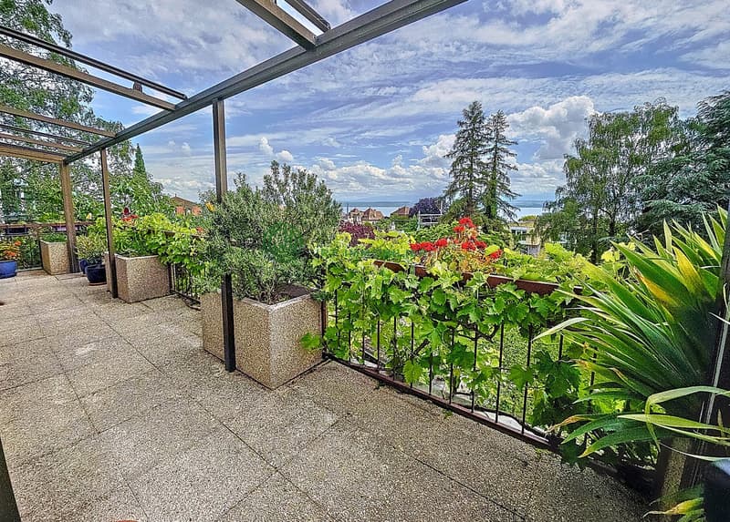 balcony with metal railing, several potted plants, pergola, lake view, blue sky