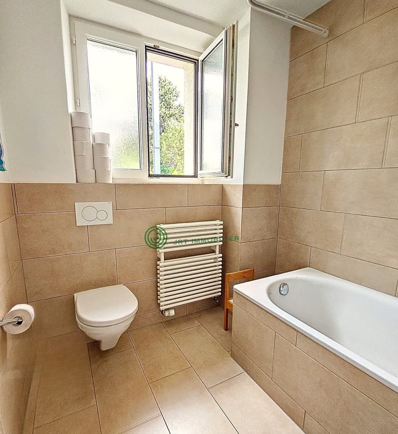 modern bathroom with white toilet, bathtub, radiator, white wall tiles, brown floor tiles