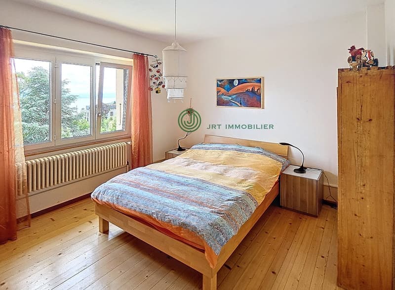 Double bed, wooden bed frame, bedside tables, floor lamp, window with curtains, radiator, painting on the wall, wooden flooring