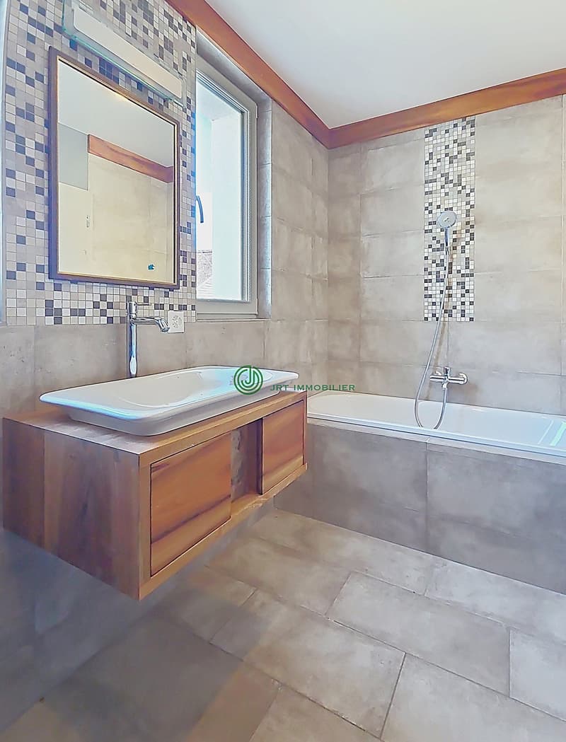 A white bathtub and sink, wall and floor tiles, a window