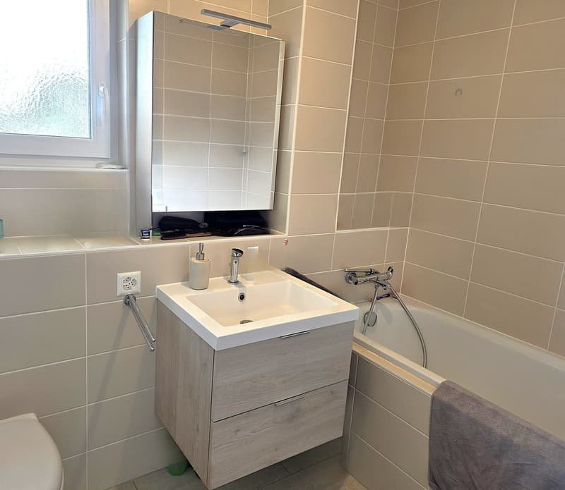 Bathroom with white tiles, white sink, mirror, bathtub, and toilet.