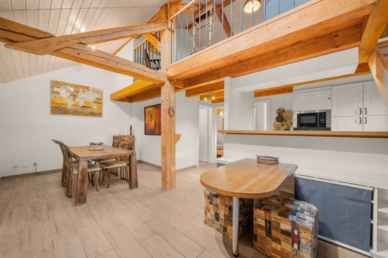 open floor plan with dining table, kitchen area with microwave, living room with wooden beams, staircase