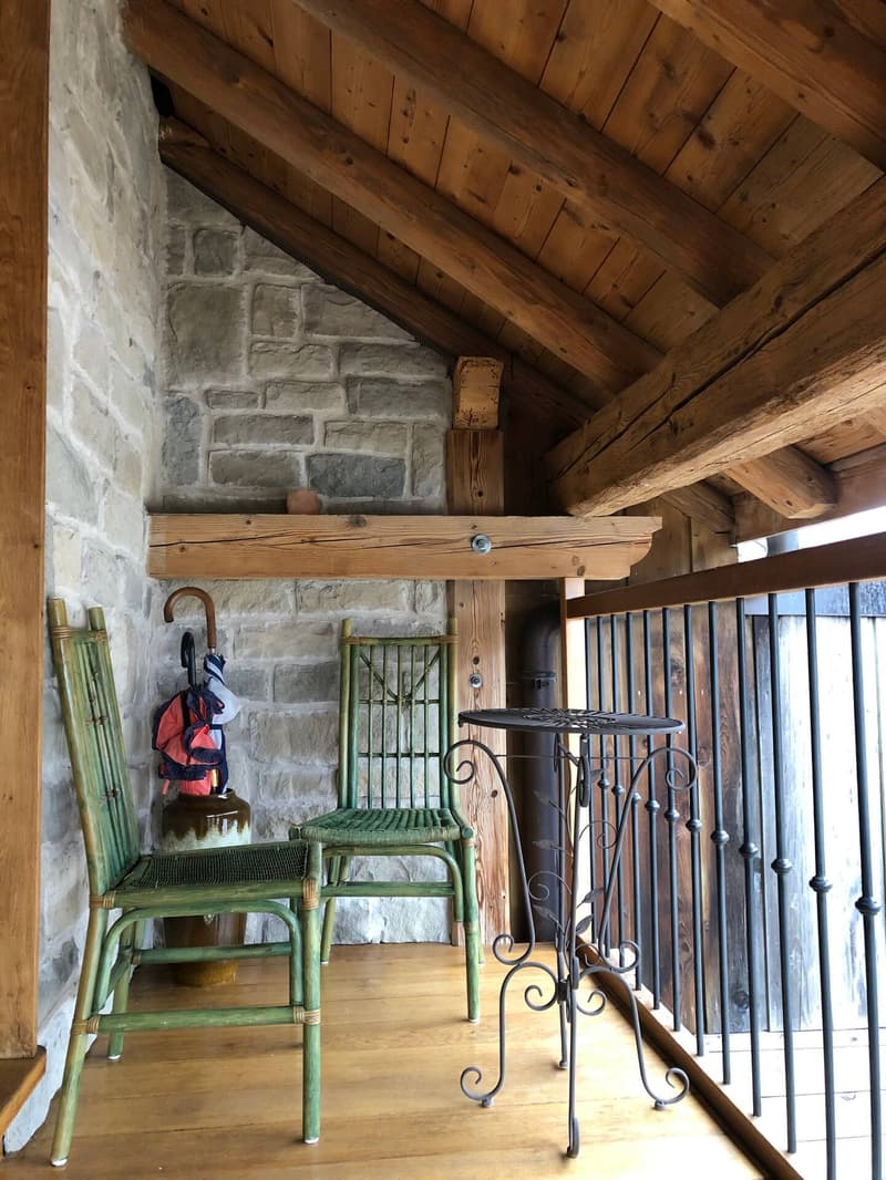 wooden ceiling, stone wall, green chairs, black table, railing