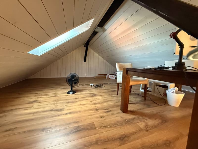 unfinished attic room, wooden flooring, white walls, fan, desk, chair, window