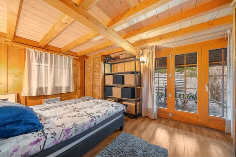 Double bed, rug, sliding doors leading to balcony, wooden ceiling, wooden floor, wardrobe, shelves with boxes, lamp