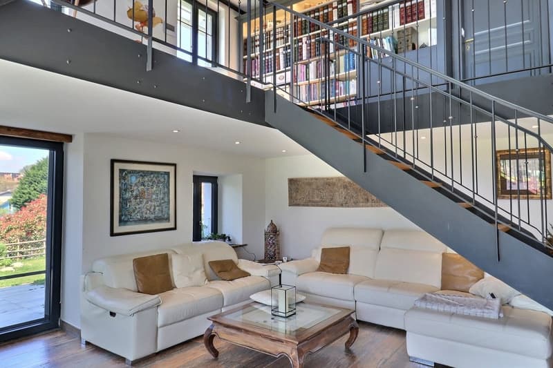 wooden floors, glass walls, two white sofas, two side tables, coffee table, two large paintings, staircase, large windows, large balcony