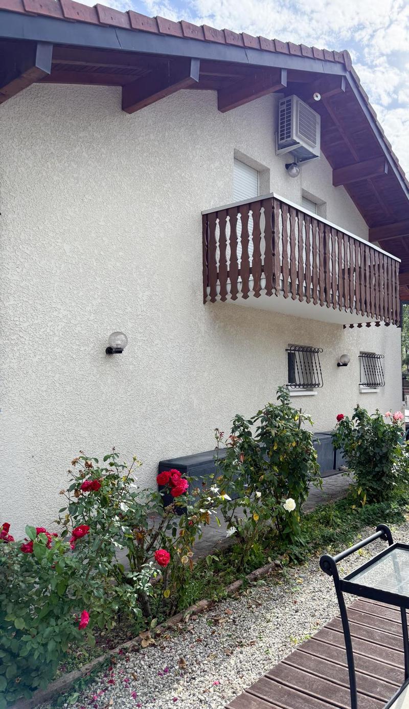 Exterior of a house with a balcony, red roof, wooden floor, white wall, small garden with flowers, air conditioner, decorative lamp