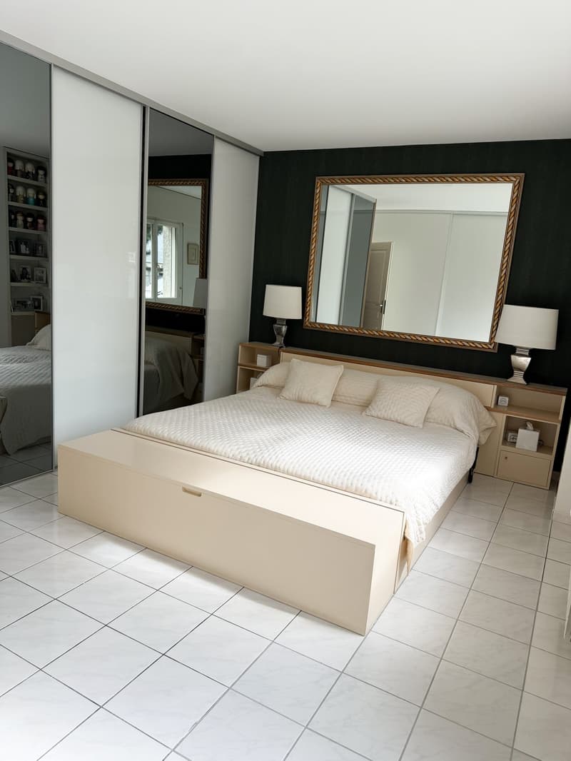 spacious bedroom with a large bed, wooden headboard, white bedding, bedside tables with lamps, large mirror, sliding wardrobes, tiled floor