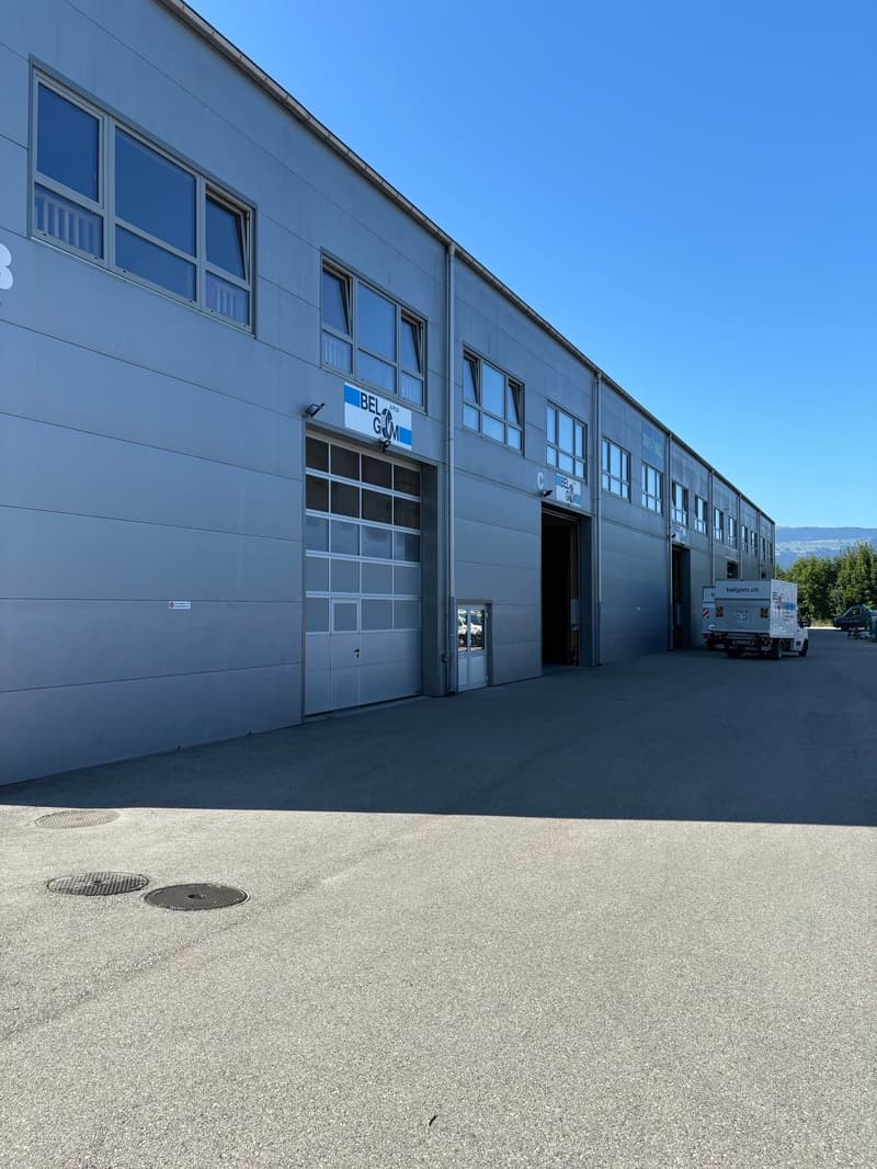 Industrial building, gray exterior, multiple windows, two large garage doors, parking area in front
