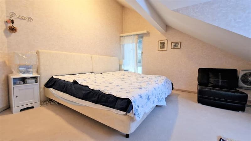 Spacious bedroom with slanted ceiling, large bed, nightstand, and a couch