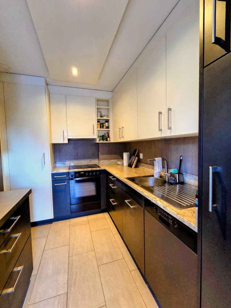 Kitchen with tiled floor, granite countertops, white cabinets, black appliances, stainless steel sink, dishwasher, open shelves, and a large window.