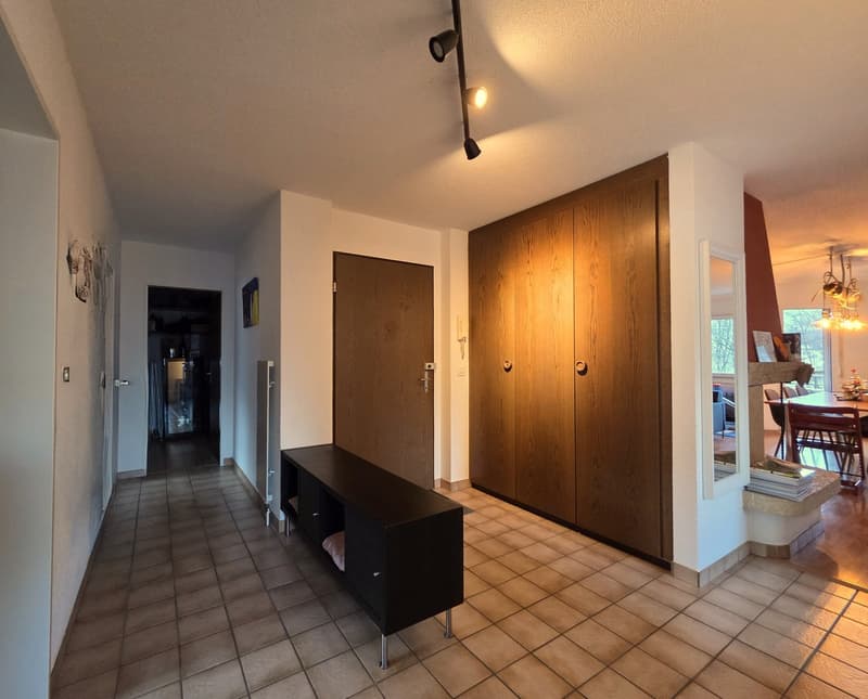 wide corridor with tiled flooring, doors, large window, mounted lamps, table, large picture frames, shelves, closet