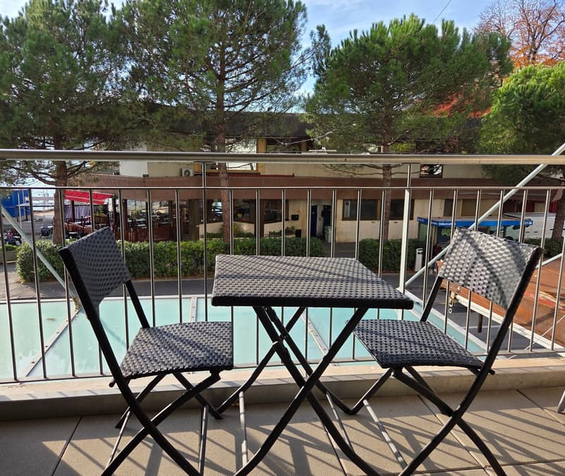 Table with 2 chairs, pool in the background, trees, swimming pool