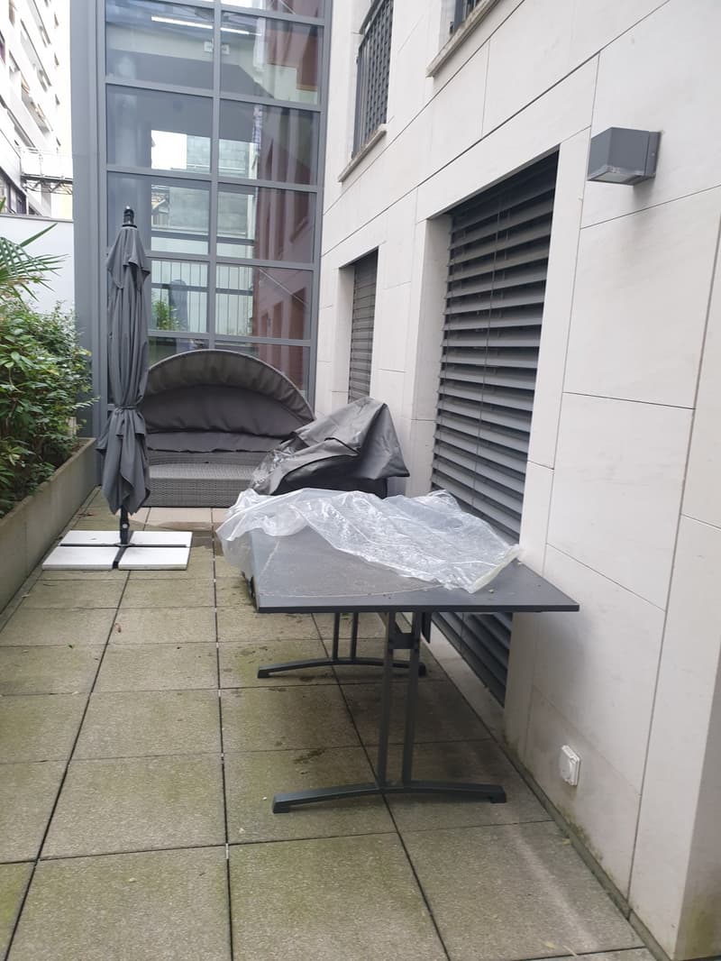 A balcony with a couch, table, umbrella, plants