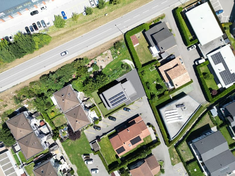 Several houses, solar panels on roofs, cars parked in front of houses, a street with a car driving, bushes and trees, and a large grassy area