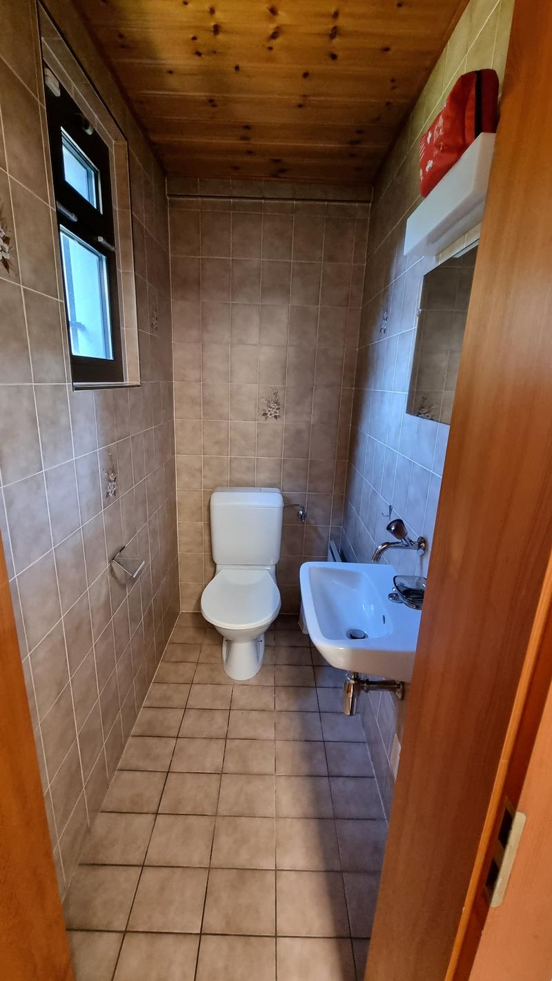 Small bathroom with tile walls, toilet, sink, window.