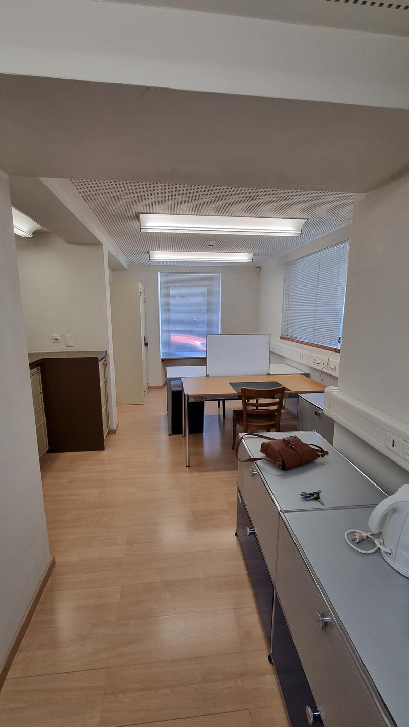 empty room, wooden floor, large windows, desk with chair, built in cabinets, open kitchen area
