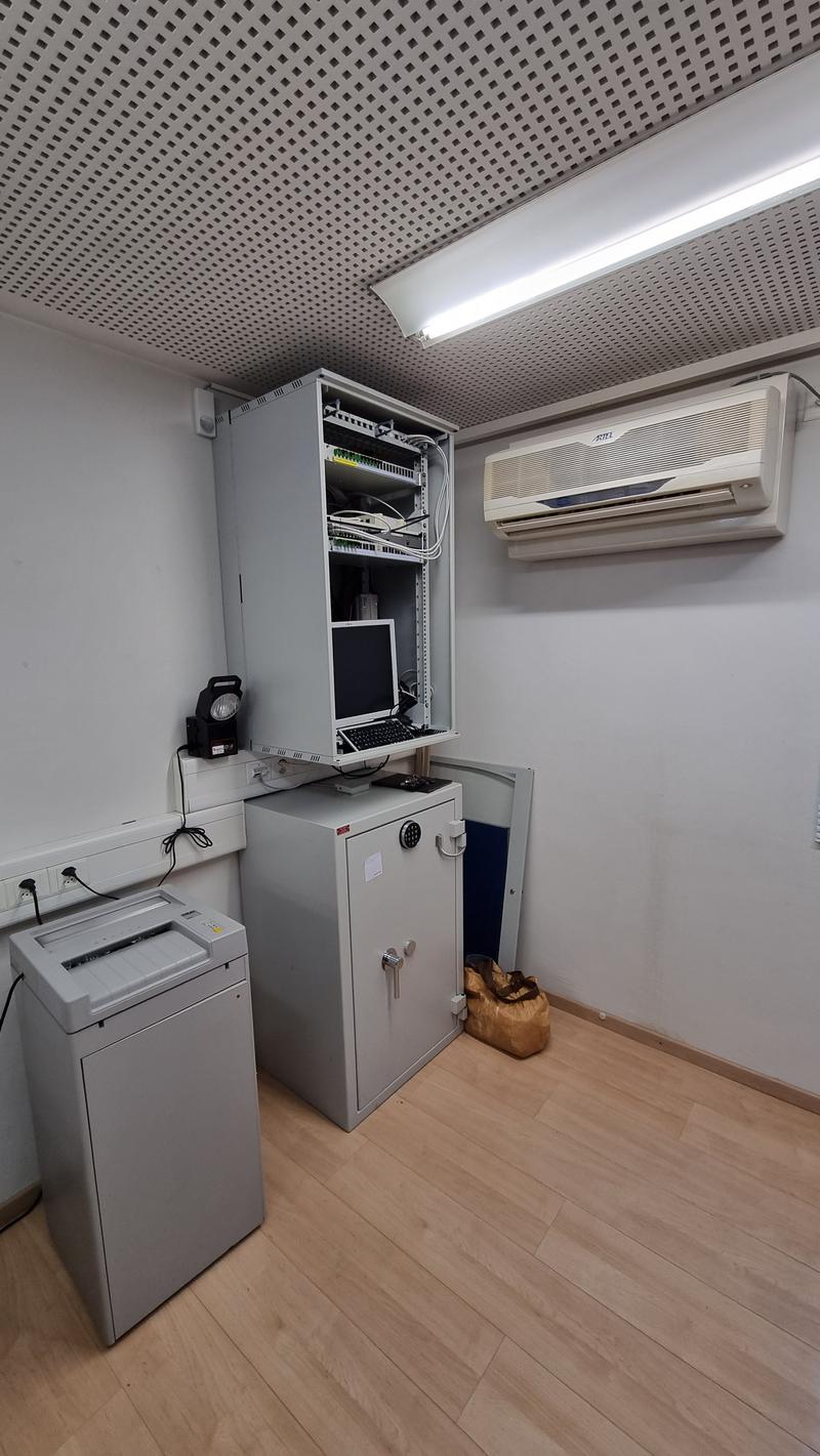 room with white walls and wooden floors, includes a computer cabinet, a metal safe, and a shredder
