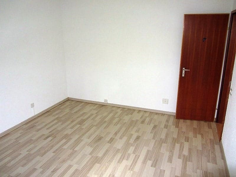 Empty room with white walls, wooden floor, and a wooden door.