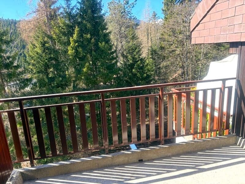 balcony with brown railings, concrete floor, shadow of railings on the floor, trees in the background