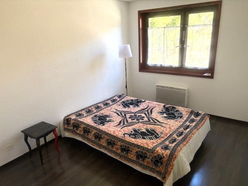 A bedroom with a bed, a lamp, a small table, a window, and a radiator