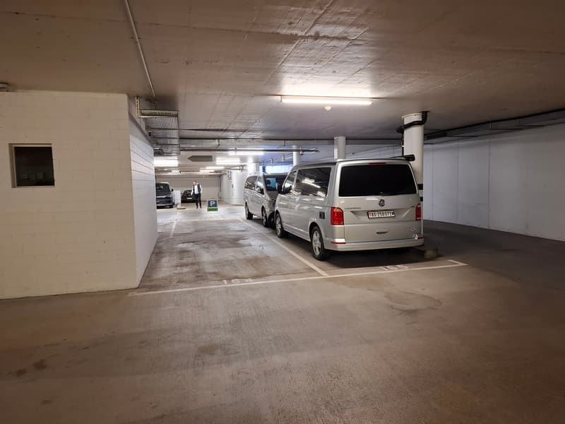 Underground parking garage with concrete floor, white walls, and parked vehicles including a silver Volkswagen van.