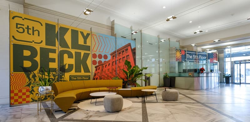 modern office lobby, yellow couch, tables, round ottomans, artwork on the wall, front desk, potted plants