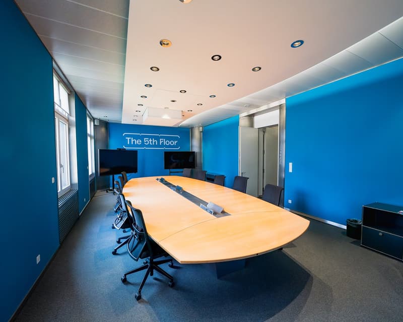 large conference table, office chairs, two monitors, blue walls, white ceiling
