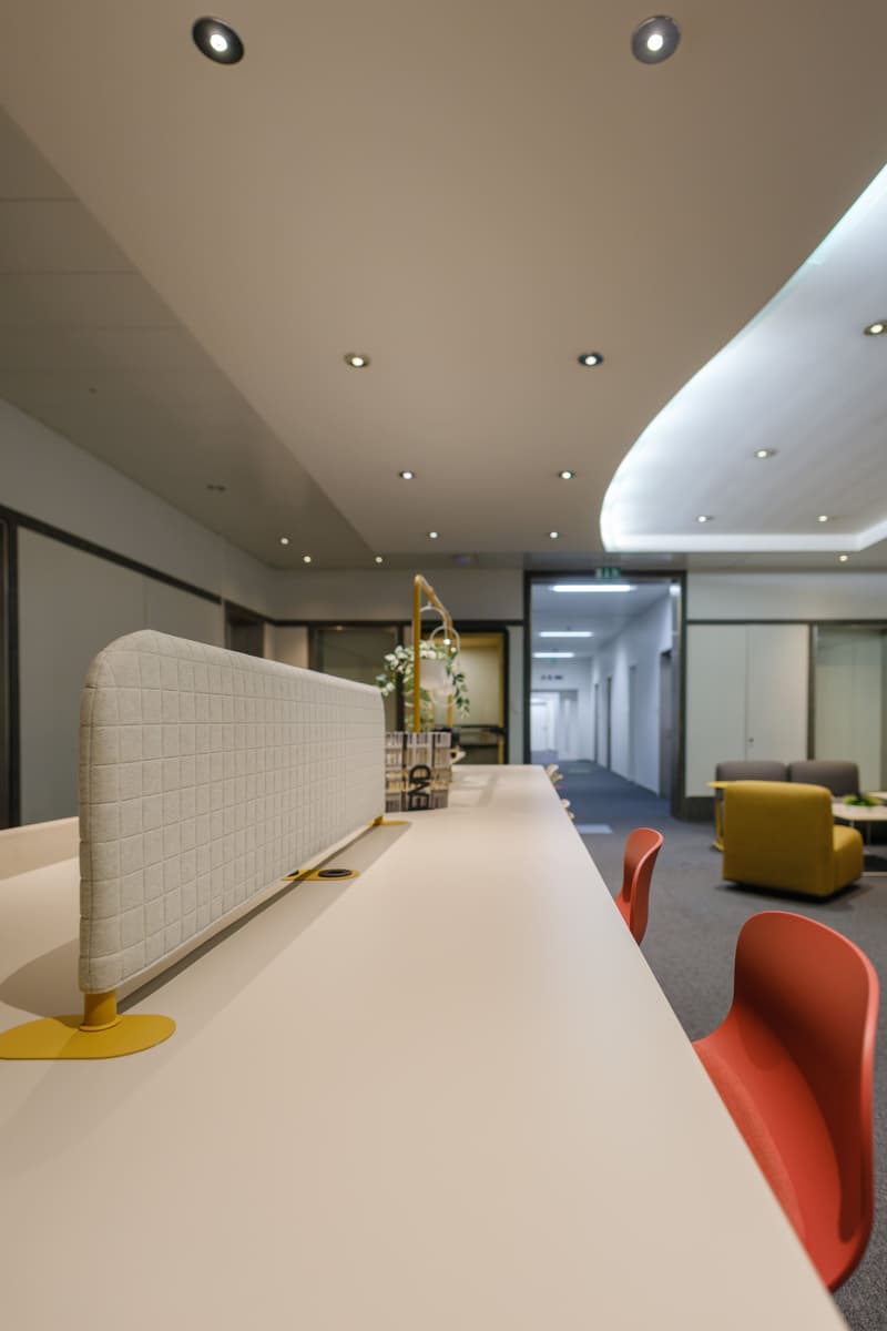 Long white desk, gray office chairs, modern decor, white ceiling, multiple lights, small yellow lamp