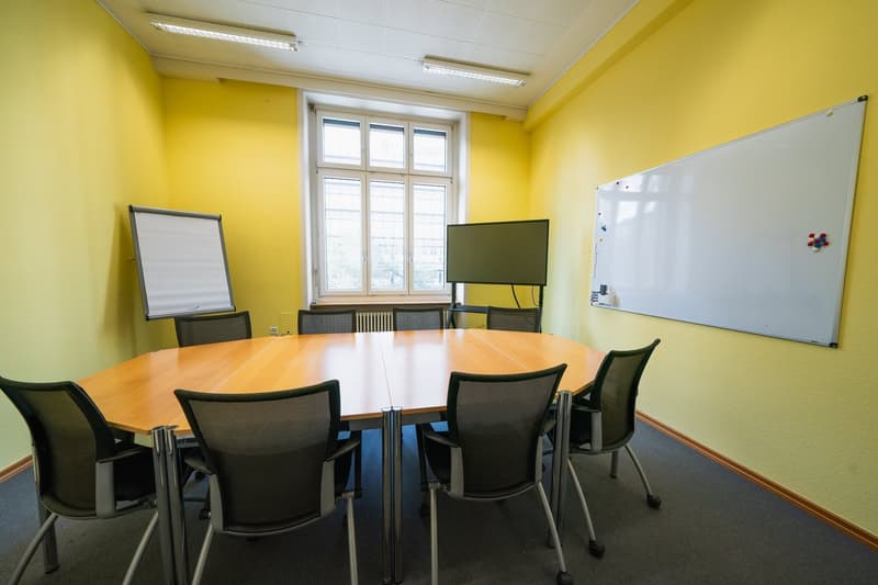 circular conference table with chairs, whiteboards, flat screen monitor, yellow walls